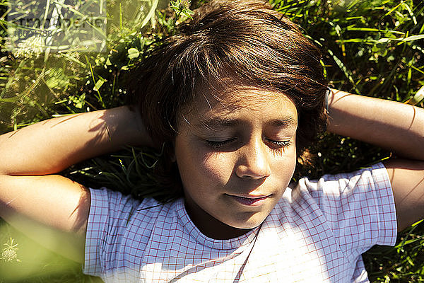 Junge mit Händen hinter dem Kopf schlafend im Gras auf einer Wiese