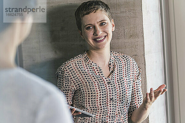 Lächelnde Unternehmerin  die mit einem Mitarbeiter im Büro diskutiert
