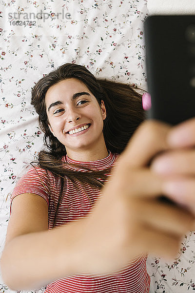 Lächelnde Frau nimmt Selfie auf Smartphone im Schlafzimmer