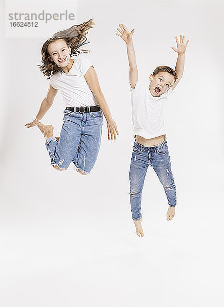 Fröhliche Geschwister springen vor weißem Hintergrund