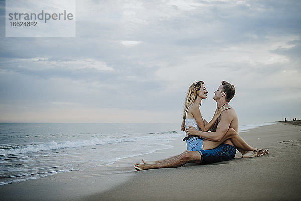 Junges Paar schaut sich am Strand sitzend an