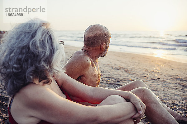 Älteres Paar bewundert den Sonnenuntergang  während es am Strand sitzt