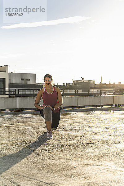 Lächelnde junge Frau beim Sport auf der Terrasse eines Gebäudes gegen den Himmel an einem sonnigen Tag