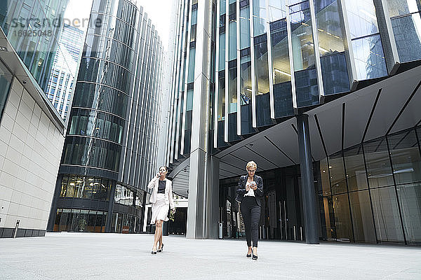 Weibliche Unternehmer zu Fuß mit Smartphones gegen Bürogebäude im Stadtzentrum in der Stadt