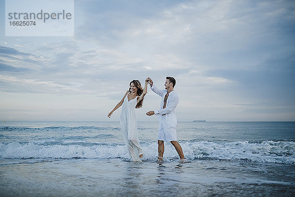 Junges Paar  das eine Frau beim Tanzen im Wasser am Strand dreht