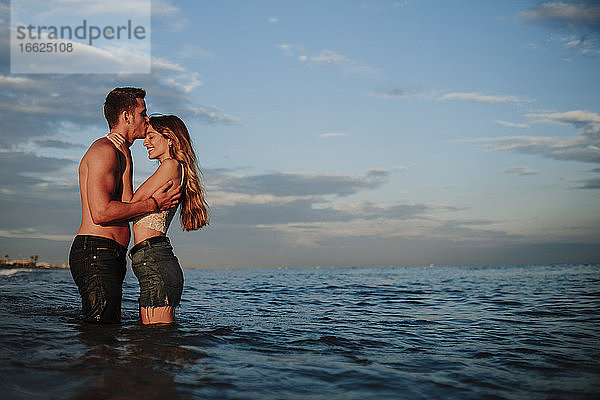 Freund küsst Freundin  während er am Strand im Wasser steht