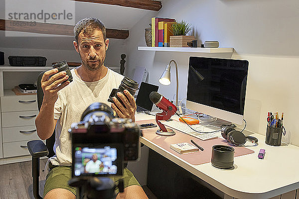 Mittlerer erwachsener Mann hält Kameraobjektive  während er zu Hause sitzt