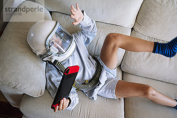 Junge mit Weltraumhelm gestikuliert beim Spielen eines Videospiels auf dem Sofa zu Hause