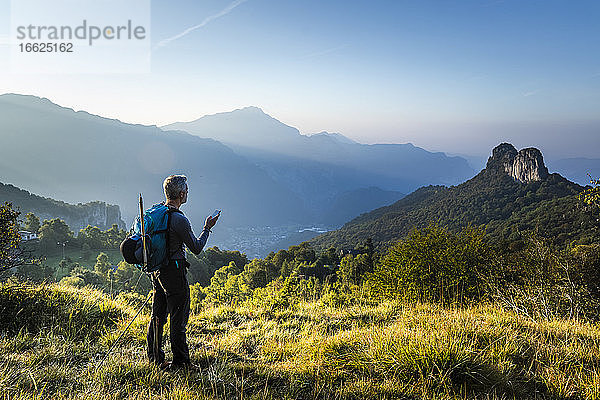 Mann mit Rucksack und Mobiltelefon auf einem Berg bei Sonnenaufgang  Orobie  Lecco  Italien