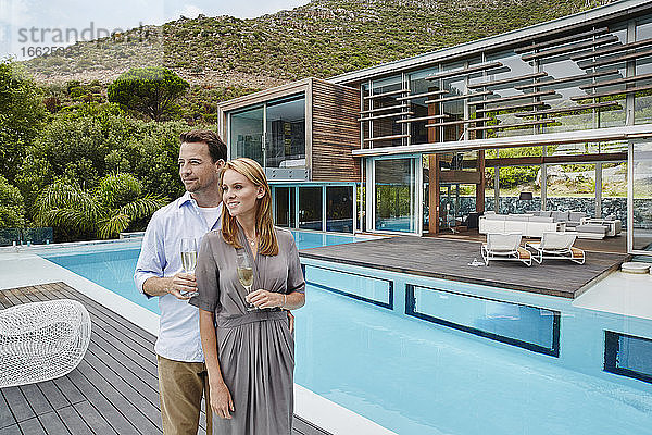 Paar hält Weinglas  während es vor einem modernen Haus steht