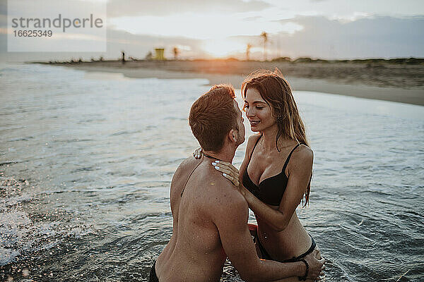 Pärchen in Badekleidung bei einer Romanze im Wasser am Strand