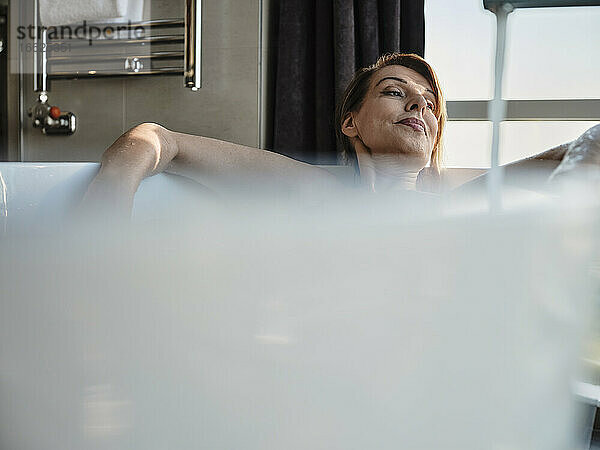 Entspannte Frau im Ruhestand nimmt ein Bad in der Badewanne vor dem Fenster eines Luxushotels