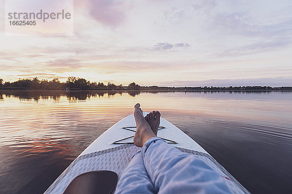 Beine einer Frau  die sich bei Sonnenuntergang auf einem Paddleboard entspannt