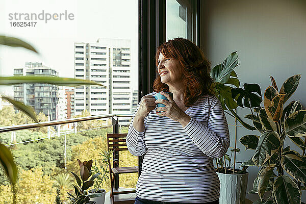 Lächelnde Frau beim Kaffeetrinken auf dem Balkon zu Hause