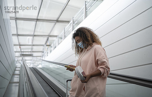 Junge Frau benutzt ein Smartphone  während sie auf einer Rolltreppe im Flughafen steht