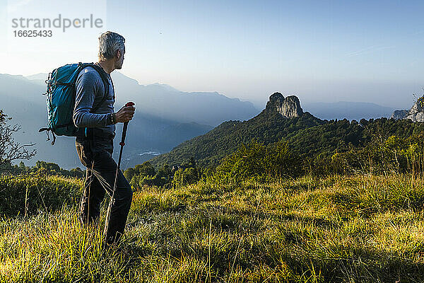 Männlicher Wanderer mit Rucksack und Stock auf einem Berg gegen den Himmel stehend  Orobie  Lecco  Italien