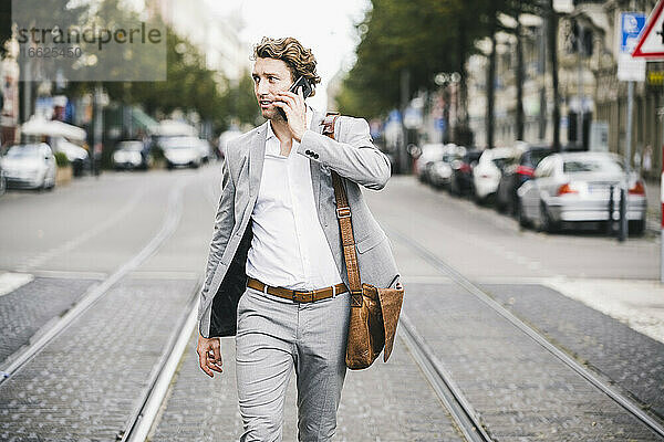 Mann mit Tasche  der in einer Straßenbahn in der Stadt mit seinem Handy telefoniert
