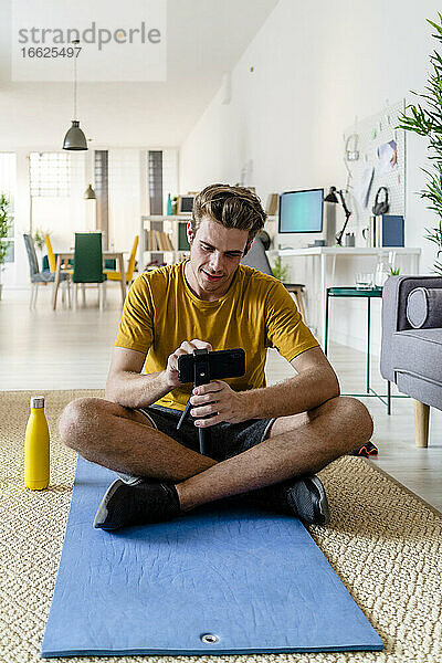 Fitnesstrainer  der zu Hause sitzend sein Mobiltelefon für Live-Streaming nutzt