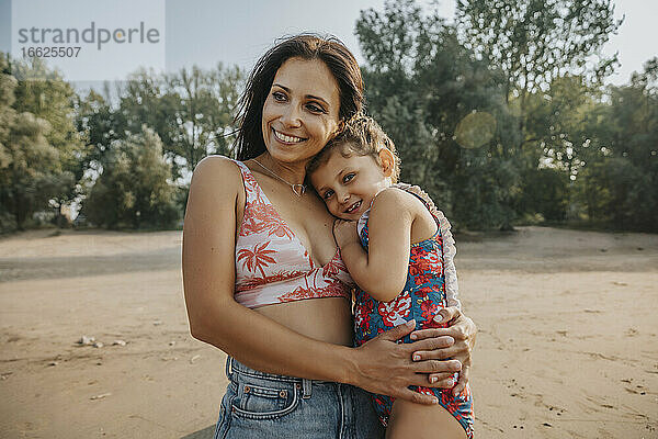 Mutter und Tochter umarmen sich  während sie am Strand stehen