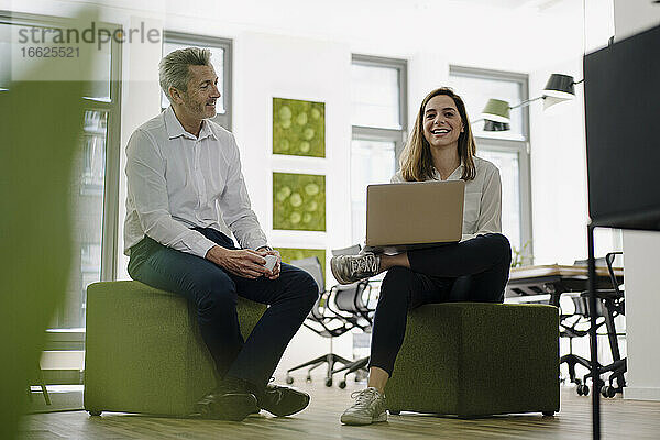 Lächelnde Partner  die einen Laptop benutzen  während sie im Büro sitzen