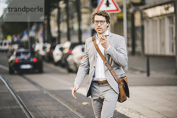 Mann mit Brille  der mit seinem Handy telefoniert  während er in einer Straßenbahn in der Stadt spazieren geht