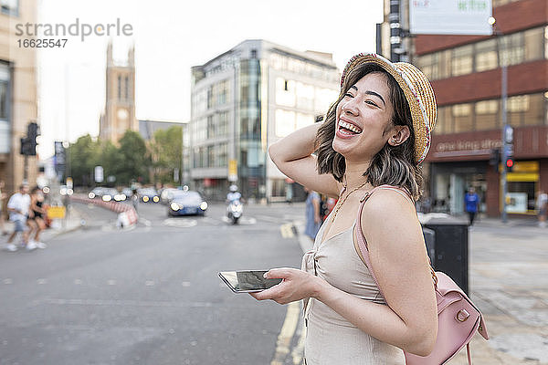 Frau lachend beim Benutzen eines Smartphones auf der Straße in der Stadt