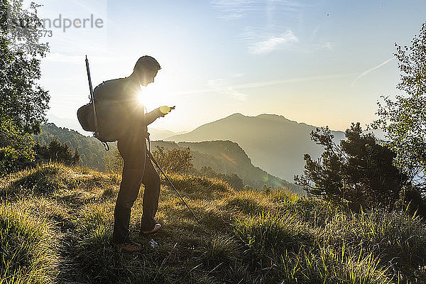 Silhouette eines Mannes  der ein Mobiltelefon benutzt  während er auf einem Berg vor dem Himmel steht  Orobie  Lecco  Italien