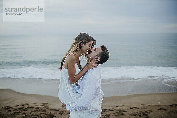 Romantisches Paar reibt sich die Nase  während es am Strand steht