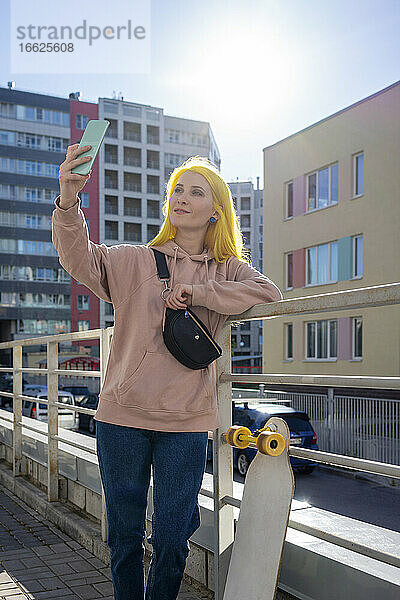 Junge Frau  die ein Selfie mit ihrem Smartphone macht  während sie an einem sonnigen Tag steht