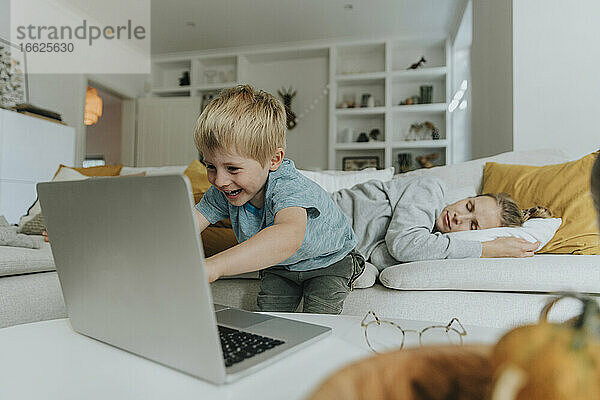 Junge benutzt Laptop bei der Mutter  die zu Hause auf dem Sofa schläft