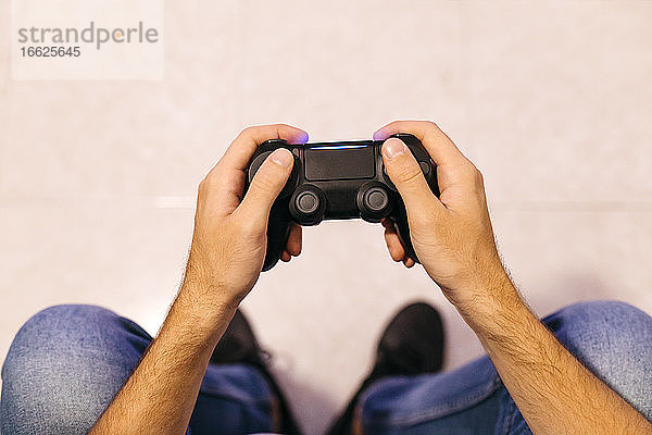 Junger männlicher Gamer hält Controller beim Spielen zu Hause