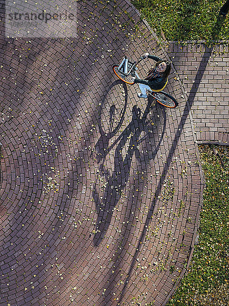 Luftaufnahme einer jungen Frau  die beim Fahrradfahren im Herbstpark zur Kamera aufschaut