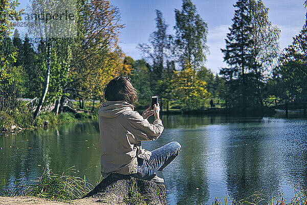Frau  die am Seeufer sitzend mit ihrem Smartphone fotografiert