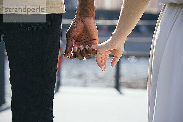 Paar hält Finger  während es auf einem Fußweg in der Stadt steht