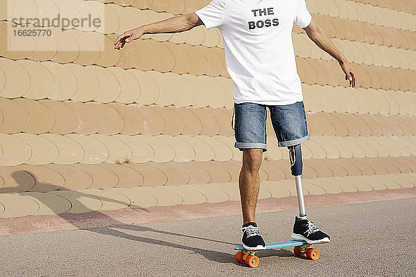 Junger Mann mit Bein- und Fußprothese steht auf einem Skateboard auf einem Sportplatz