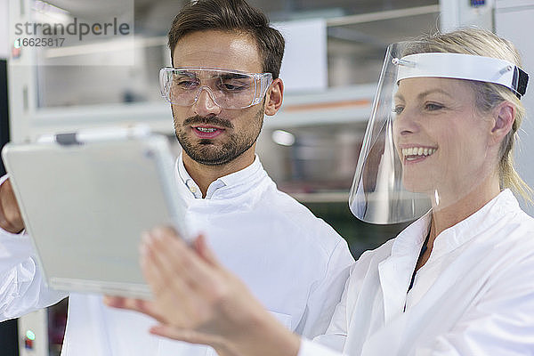 Männliche und weibliche Techniker diskutieren über einem digitalen Tablet in einem beleuchteten Labor