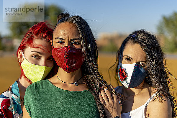 Freunde tragen eine bunte Gesichtsmaske  während sie an einem sonnigen Tag im Freien stehen