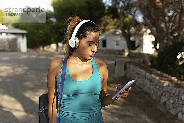 Junge hispanische Frau  die ein Smartphone benutzt und Musik hört