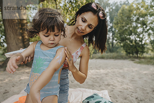 Mutter trägt Sonnenschutzmittel auf ihre Tochter am Strand auf