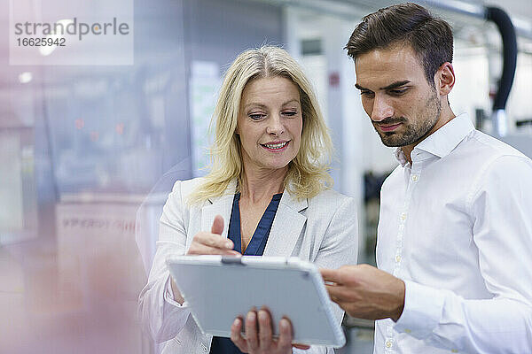 Blonde Geschäftsfrau  die mit einem jungen männlichen Kollegen in einer Fabrik über ein digitales Tablet diskutiert