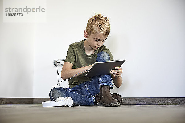 Kleiner Junge spielt auf einem digitalen Tablet  während er in einem neuen Haus sitzt