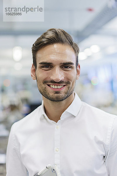 Lächelnder junger männlicher Ingenieur vor einer beleuchteten Fabrik