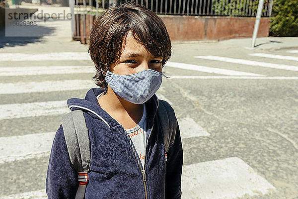 Schuljunge mit Maske auf der Straße an einem sonnigen Tag