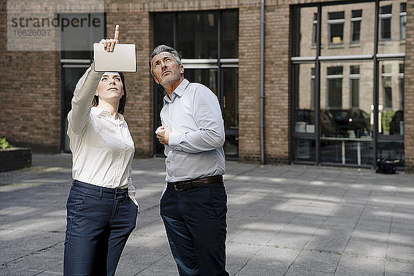 Geschäftsfrau  die nach oben zeigt  während sie neben einem Mann an einem Gebäude steht