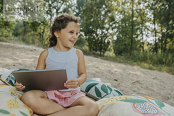 Lächelndes süßes Mädchen  das wegschaut und ein digitales Tablet hält