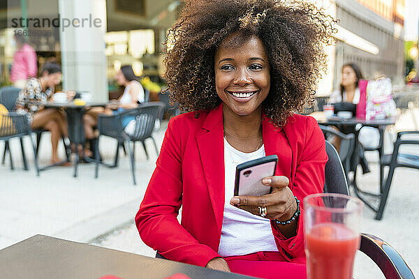 Lächelnde Frau  die in einem Straßencafé sitzt und SMS schreibt