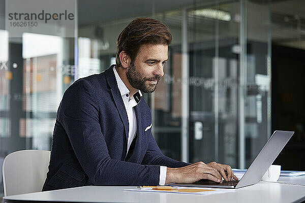 Geschäftsmann arbeitet am Laptop  während er im Büro sitzt