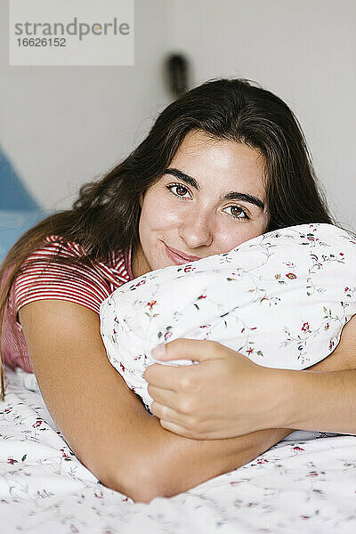 Lächelnde Frau mit Kissen auf dem Bett liegend zu Hause im Schlafzimmer