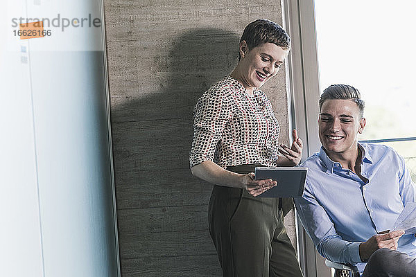 Lächelnde Unternehmerin  die mit einem Geschäftsmann im Büro über ein digitales Tablet diskutiert