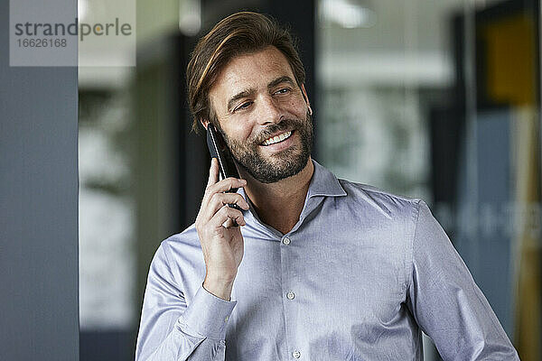 Lächelnder Geschäftsmann  der im Büro mit seinem Handy telefoniert
